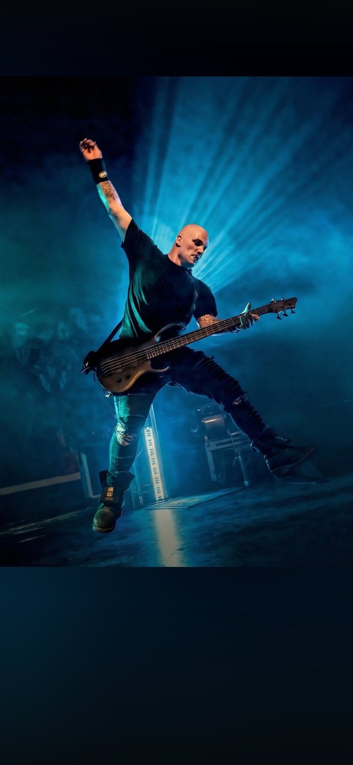 Dean mid-air on stage with his bass, fist raised