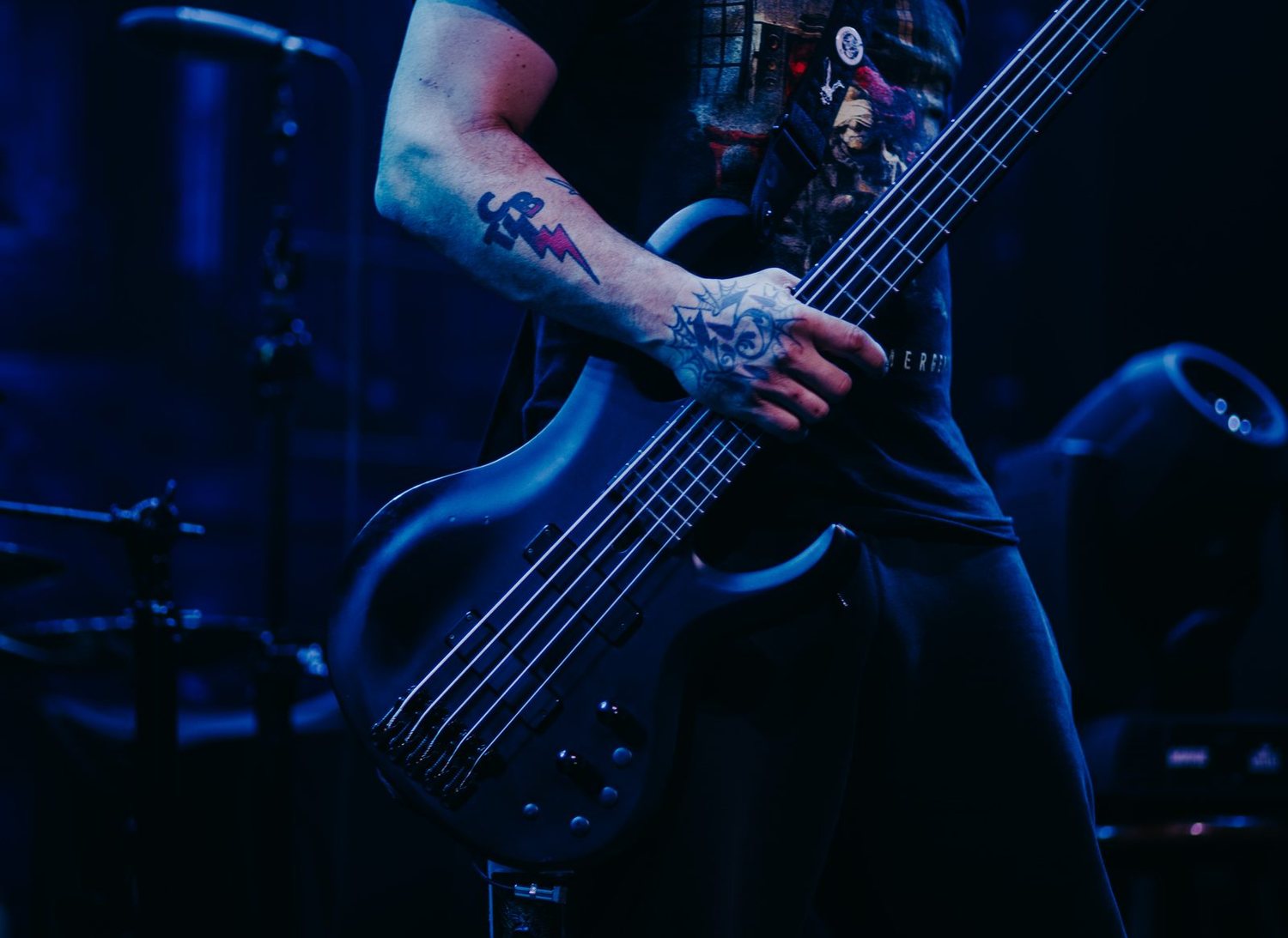Close on a five-string fretboard under blue stage light, left hand mid-phrase
