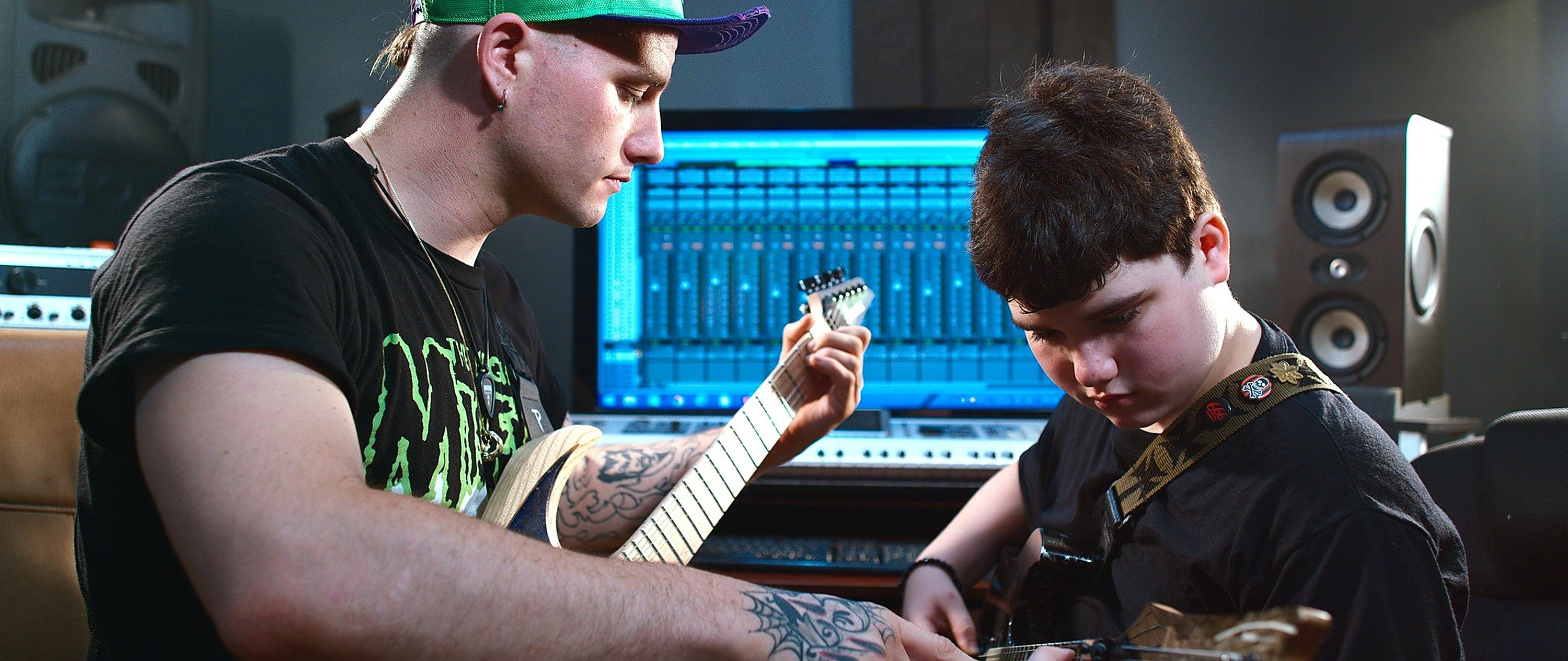 Dean working through a part with a young student in the studio, a DAW session open on the screen behind them