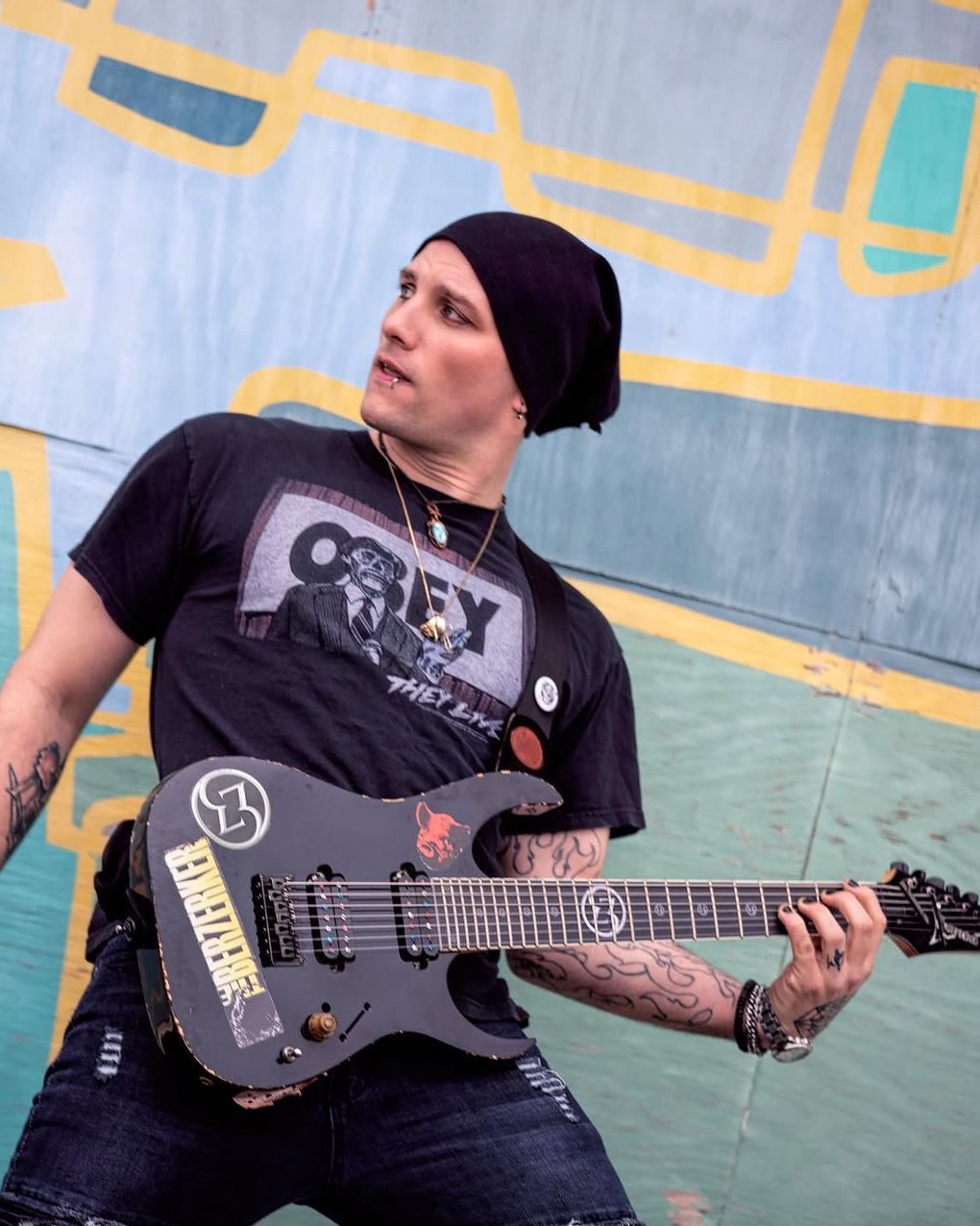 Dean outside against a painted wall with a black eight-string Ibanez