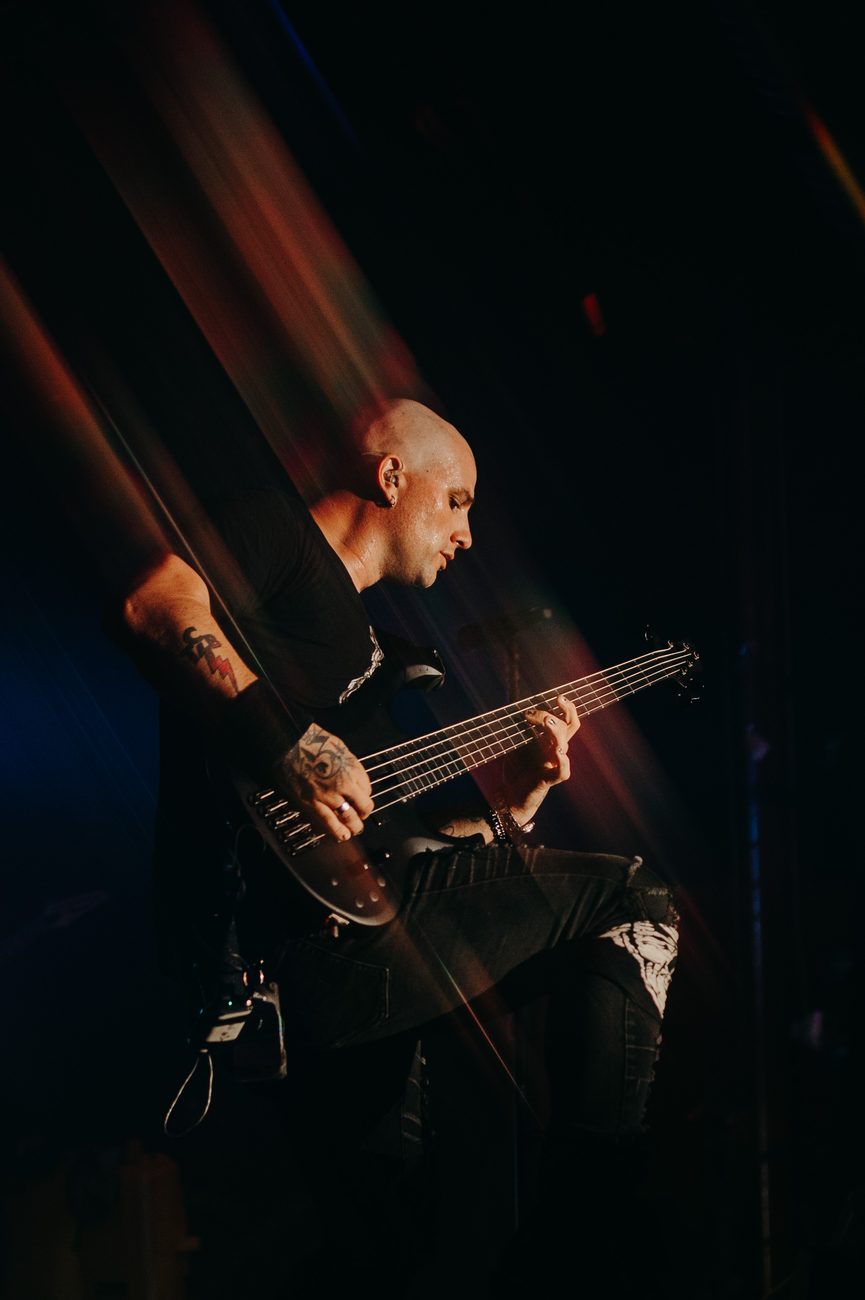 Dean on stage with his five-string, cut through by beams of stage light