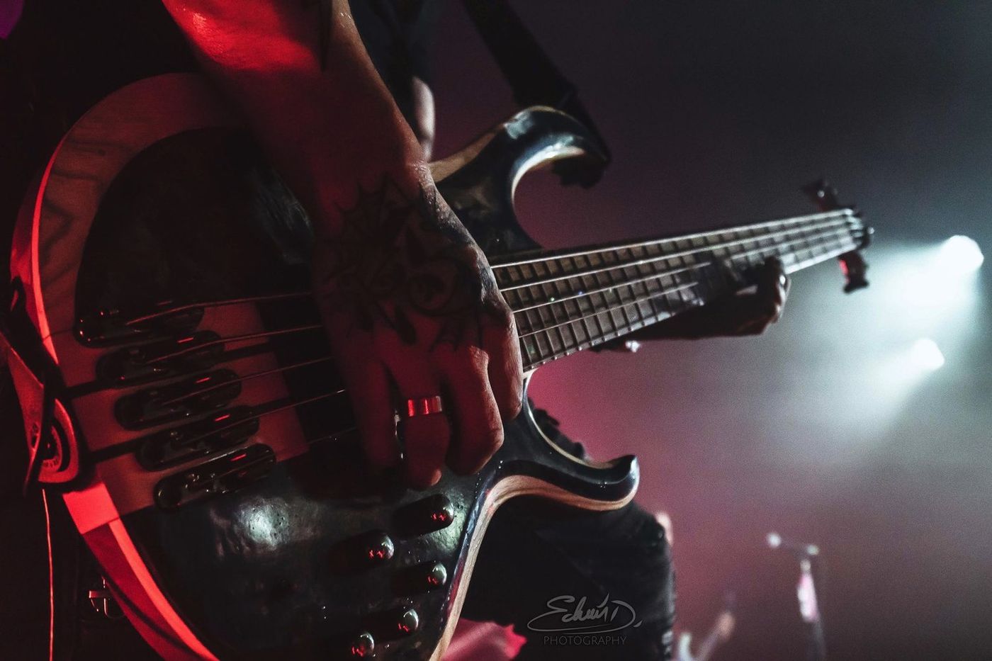 Close on Dean's hands playing his five-string under red stage light