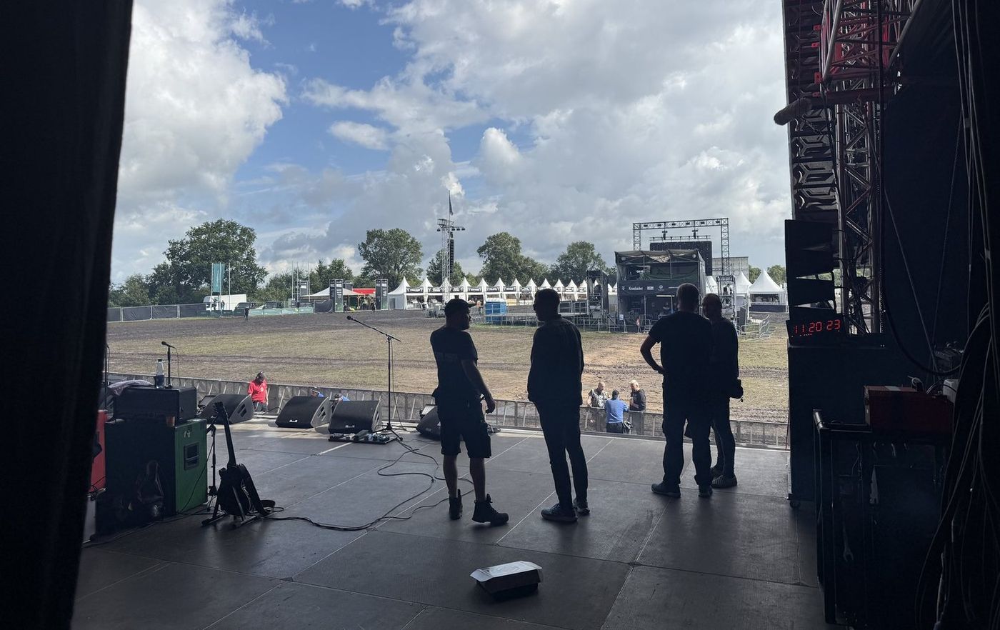 The view out from a festival stage before doors: empty field, crew checking the deck